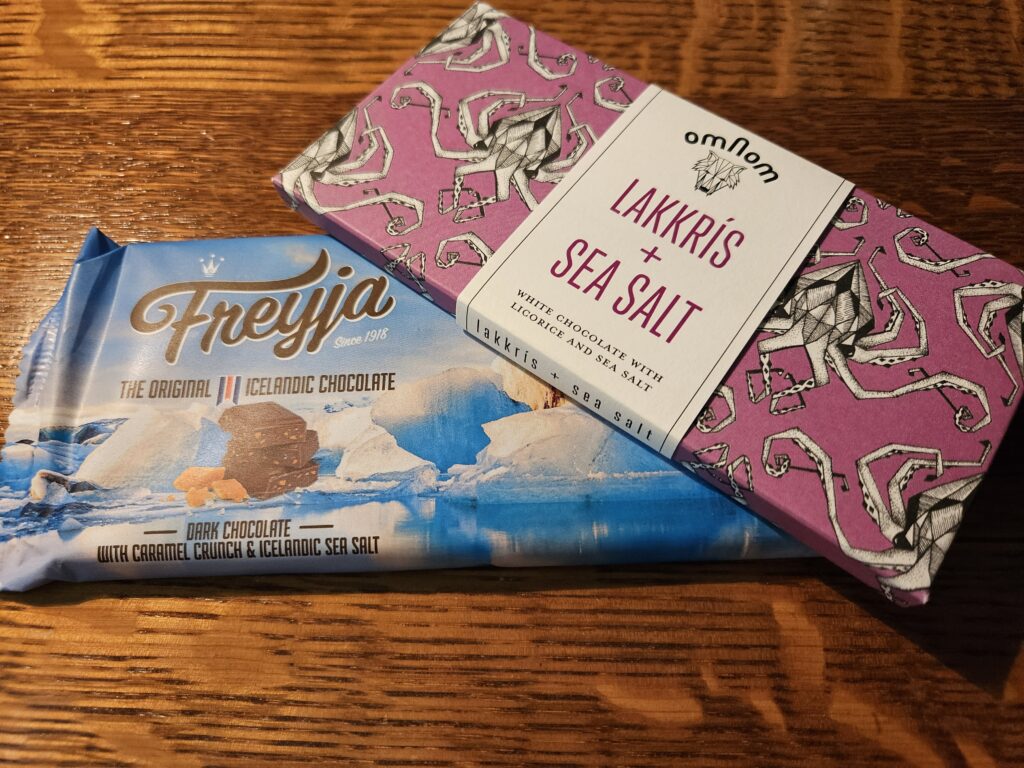 Sweet Seat Swap Two Icelandic chocolate bars: a Freyja dark chocolate with caramel crunch and sea salt, and an Omnom Lakkrís + Sea Salt white chocolate bar.